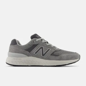 Grå New Balance-sneaker med mocka- och meshdetaljer, sula med hexagonmönster och texten "Fresh Foam" på sidan. Skon visar snörning och ett stort N-logotyp på sidopanelen. Designad för komfort och stil.